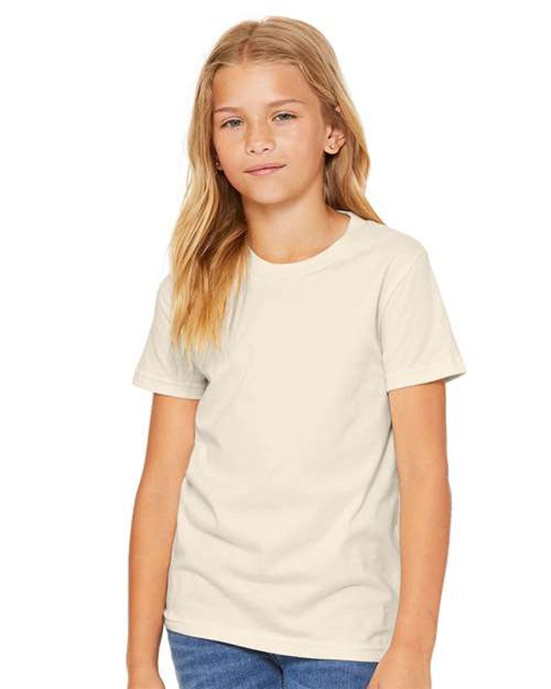 May include: A young person wearing a plain, off-white short-sleeved t-shirt. The t-shirt has a crew neck and is made of a soft, comfortable fabric.