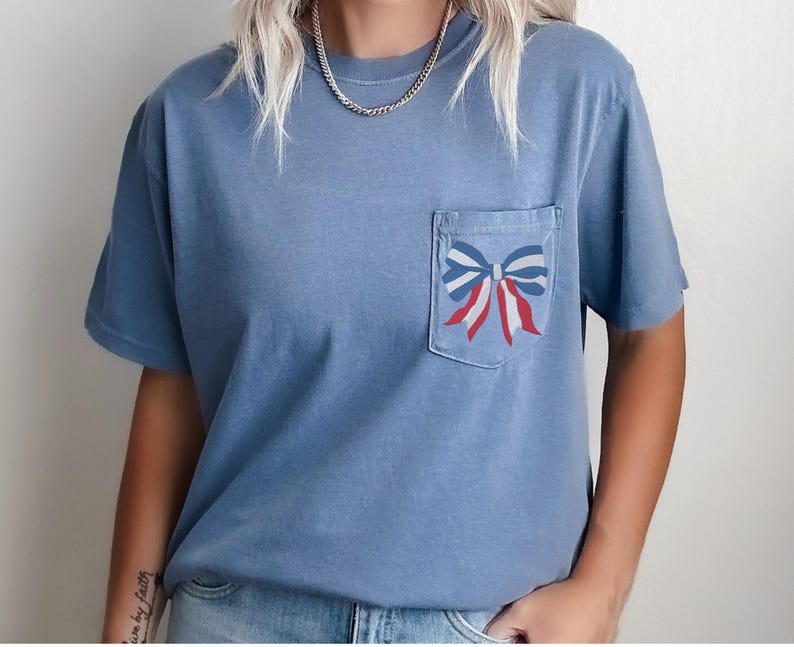 Pode incluir: Uma camiseta azul claro com um la&ccedil;o vermelho, branco e azul em um bolso.
