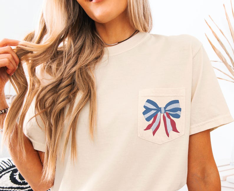 Pode incluir: Uma camiseta bege com um la&ccedil;o vermelho, branco e azul no bolso.