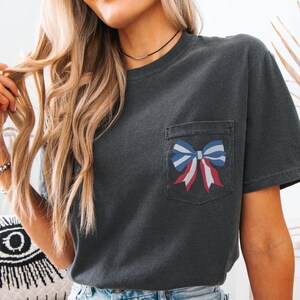 Pode incluir: Uma camiseta cinza escura com um la&ccedil;o vermelho, branco e azul em um bolso na frente.