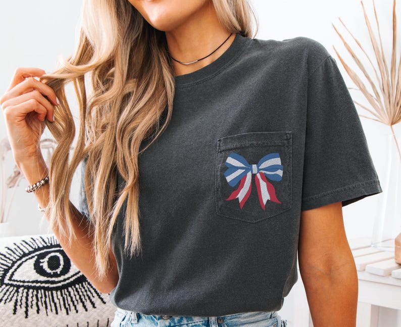 Pode incluir: Uma camiseta cinza escura com um la&ccedil;o vermelho, branco e azul em um bolso na frente.