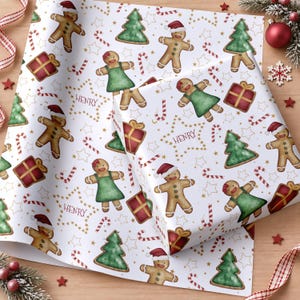 May include: White wrapping paper featuring a repeating pattern of gingerbread people wearing red hats, gingerbread people in green dresses, green Christmas trees, red gift boxes with gold ribbons, candy canes, and the name HENRY in gold stars.