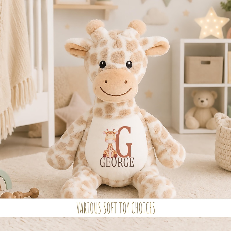 May include: A plush giraffe toy with a cream and tan spotted pattern, featuring a white belly patch printed with a small giraffe illustration, the letter G, and the name GEORGE in dark brown text, with black embroidered eyes and a stitched smile.