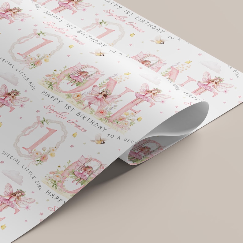 May include: White wrapping paper featuring a repeating pattern of pink fairies, floral arrangements, and the number one. The text reads Happy 1st Birthday to a very special little girl and the name Sophia Grace in a cursive pink script font.