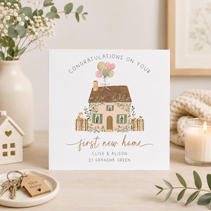 May include: A square greeting card with a white background featuring a watercolour illustration of a pink house with a brown roof, green shutters, and a wooden fence. Text reads: CONGRATULATIONS ON YOUR first new home CLIVE & ALISON 21 GRANSHA GREEN.