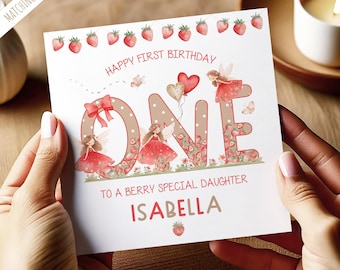 May include: A birthday card with the text "Happy First Birthday" and "One" in large letters, decorated with strawberries, fairies, and the name "Isabella". The card has a berry theme with a bow and heart-shaped balloons.