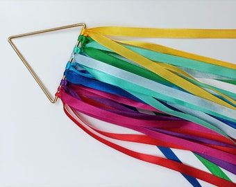 May include: A gold triangle-shaped metal frame with rainbow colored satin ribbons tied to it. The ribbons are arranged in a rainbow pattern, with red, orange, yellow, green, blue, indigo, and violet ribbons.