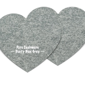 Puede incluir: Dos parches de tela de cachemira gris en forma de corazón con el texto "Pure Cashmere - Dusty Blue Grey -" impreso en blanco.