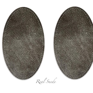 Puede incluir: Dos parches ovalados de ante gris oscuro con agujeros de costura preperforados a lo largo del per&iacute;metro. Los parches tienen una superficie texturizada y el texto Real Suede est&aacute; impreso en fuente cursiva bajo las dos formas ovaladas.