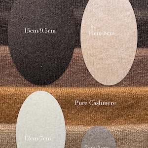 Può includere: Quattro toppe in tessuto di forma ovale in nero, beige, grigio chiaro e grigio scuro, sovrapposte a un tessuto a maglia marrone e marrone chiaro. Le toppe riportano le dimensioni: 15cm per 9,5cm, 14cm per 8cm, 12cm per 7cm e 7cm per 5cm. Testo: Pure Cashmere.