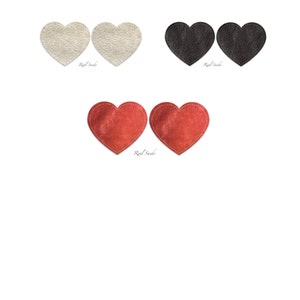Può includere: Due paia di toppe in pelle scamosciata a forma di cuore in bianco, nero e rosso. Le toppe sono cucite sui bordi e hanno le parole "Real Suede" stampate sotto.