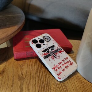 May include: White iPhone case with a red and black graphic design. The design features a firefly, the words "Endure Survive", and the text "When you're lost in the darkness look for the light".