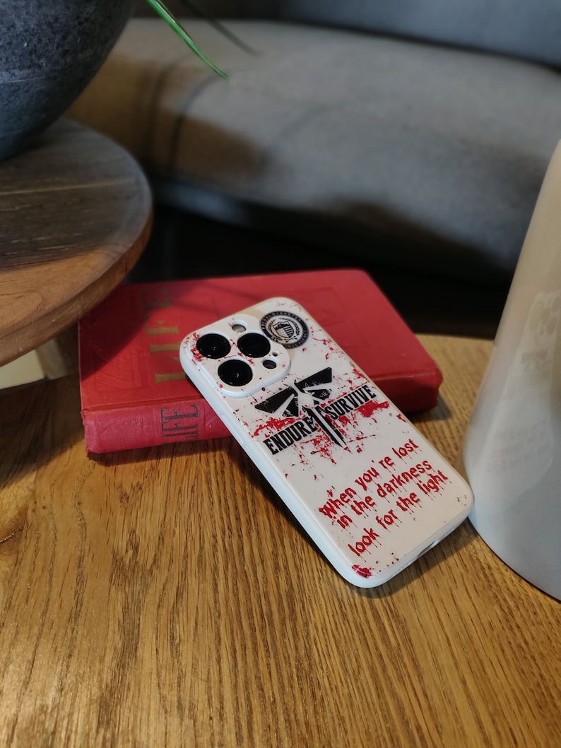 May include: White iPhone case with a red and black graphic design. The design features a firefly, the words "Endure Survive", and the text "When you're lost in the darkness look for the light".