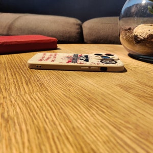 May include: A white phone case with a red and black graphic design. The design features a skull and crossbones with the text "May the odds be ever in your favour".