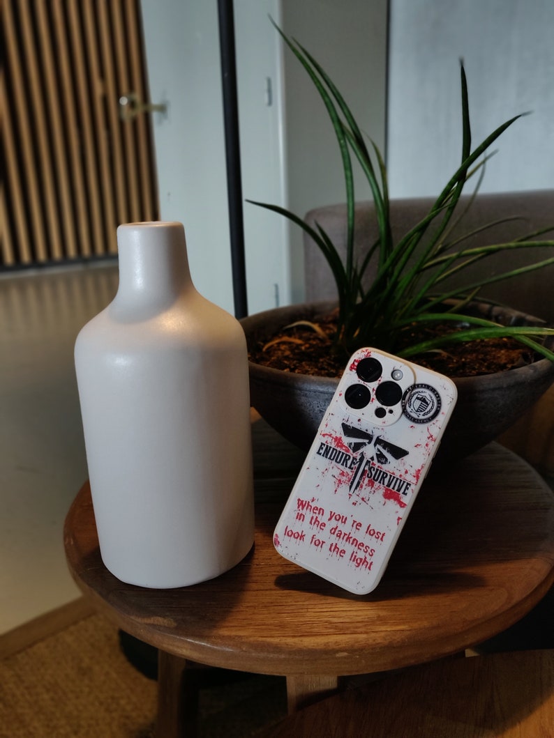 May include: White phone case with a red and black graphic design. The design features a firefly, the words "Endure" and "Survive", and the text "When you're lost in the darkness look for the light".