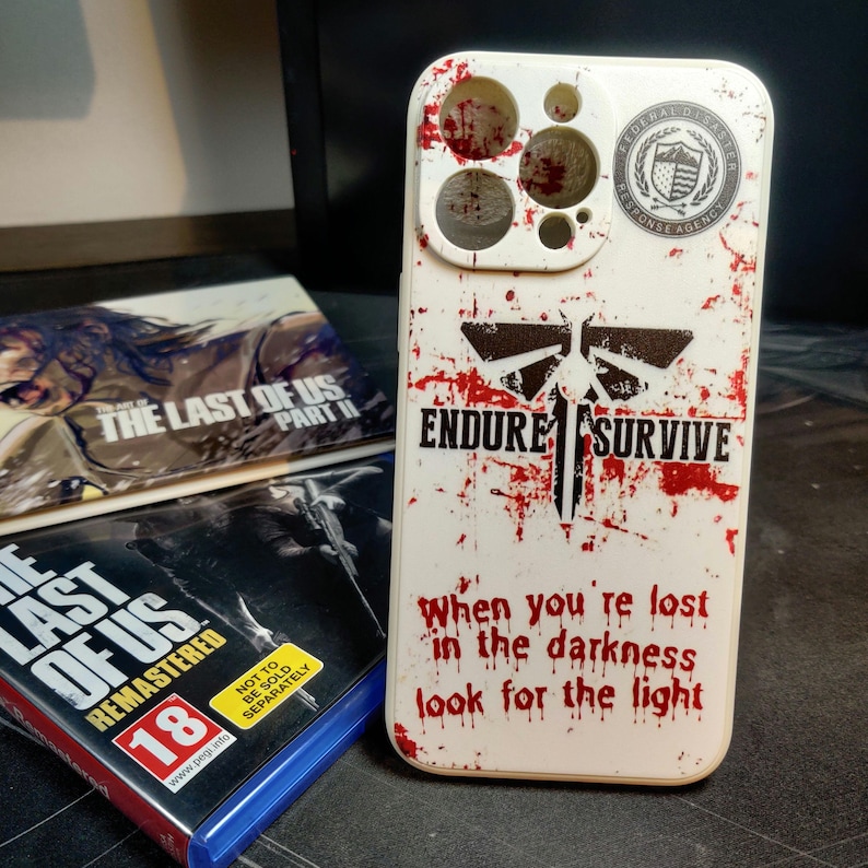 May include: White iPhone case featuring a red and black graphic of a firefly with the words "Endure" and "Survive" printed on it. The case also has a red and white splatter pattern and the words "When you're lost in the darkness look for the light".