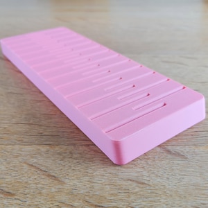 May include: A pink plastic storage box with multiple compartments. The box is designed to hold small items, such as jewellery or craft supplies.