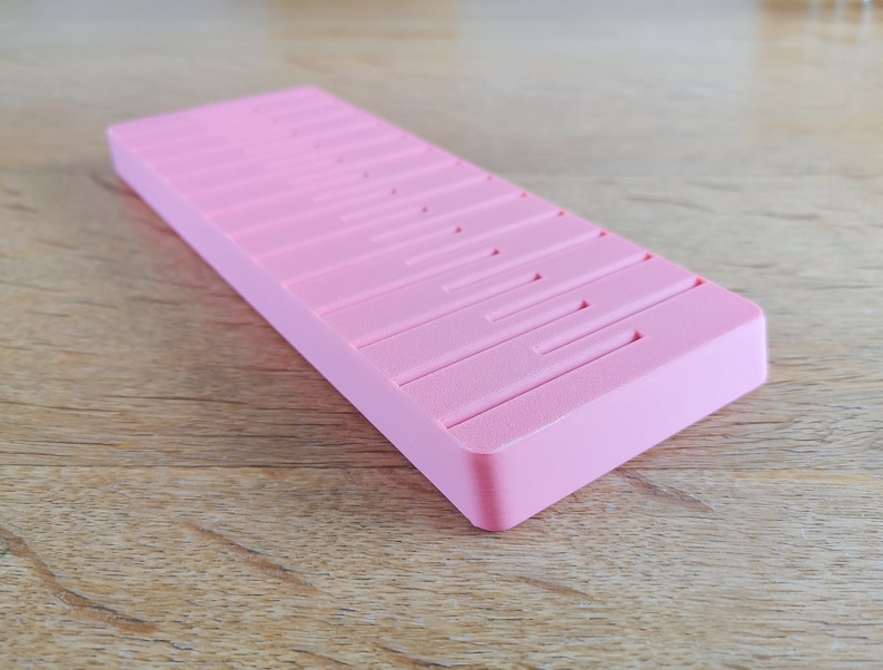 May include: A pink plastic storage box with multiple compartments. The box is designed to hold small items, such as jewellery or craft supplies.