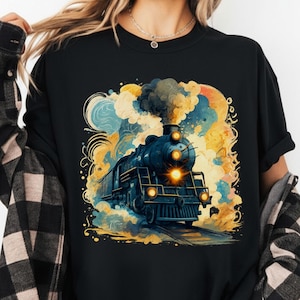 Peut inclure: T-shirt noir à col rond avec une illustration colorée d'un train à vapeur vintage. Le train est bleu foncé avec des phares jaunes, sur fond de nuages tourbillonnants jaunes, bleus et oranges. Le t-shirt est porté par une personne.