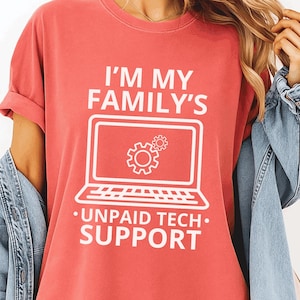 Peut inclure: T-shirt de couleur pastèque avec l'inscription blanche "I'M MY FAMILY'S UNPAID TECH SUPPORT". Le graphisme représente un ordinateur portable avec des icônes d'engrenages. Le t-shirt a des manches courtes et un col rond. Une veste en jean est drapée sur les épaules.