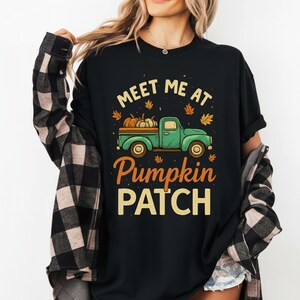Peut inclure: T-shirt noir avec un motif sur le thème de l'automne. Le design présente un pick-up vert d'eau transportant des citrouilles, avec le texte "Meet Me At Pumpkin Patch" en jaune et orange. Des feuilles d'automne sont éparpillées.