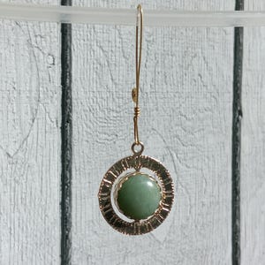 May include: Gold dangle earrings with a green stone set in a circular wire frame.