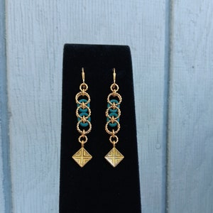 May include: Gold earrings with a turquoise chain and a gold square pendant.
