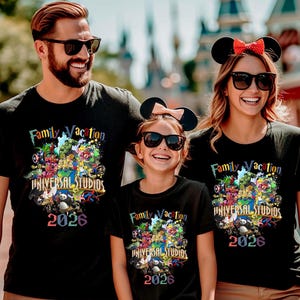 May include: Three black t-shirts featuring a colorful graphic print with the text Family Vacation, Universal Studios, and 2026. The design includes various animated characters, and the shirts are worn by three individuals with sunglasses.