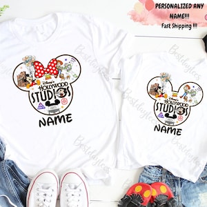 May include: Two white t-shirts with a Mickey Mouse head design featuring Disney's Hollywood Studios logo. The design includes various Disney characters like Mickey Mouse, Minnie Mouse, Woody, Buzz Lightyear, and others. The text "Disney's Hollywood Studios" and "NAME" are printed on the shirts.