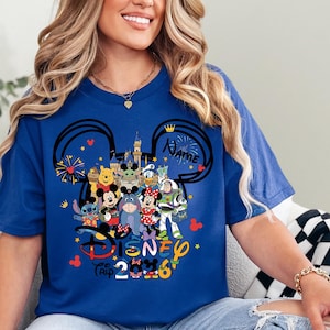 Peut inclure: T-shirt bleu roi avec un motif Disney Trip 2026. Le motif comprend des oreilles de Mickey Mouse, un ch&acirc;teau et divers personnages Disney tels que Mickey, Minnie et Winnie l'ourson. Le mot "Name" est &eacute;galement inclus.