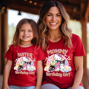 May include: Red t-shirts with a colorful graphic featuring Hello Kitty and friends. One shirt says "Sister of the Birthday Girl" and the other says "Mommy of the Birthday Girl". The shirts are worn by a mother and daughter.