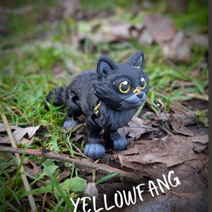 以下が含まれることがあります： 葉と草の上に置かれた、黄色い目とアクセントのある黒い猫の置物。画像の下部には白で「YELLOWFANG」という文字が表示されています。猫は詳細で質感のある外観をしています。