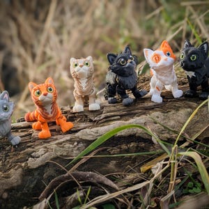 以下が含まれることがあります： さまざまな色（グレー、オレンジ、黒、白など）の6つの猫の置物のコレクションが、風化した丸太の上に配置されています。 置物には詳細な特徴があり、さまざまなポーズをとっており、遊び心のある気まぐれなシーンを作り出しています。