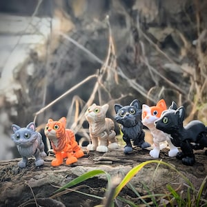 以下が含まれることがあります： グレー、オレンジ、タン、黒、白など、さまざまな色の7つの猫の置物のコレクションが、風化した丸太の上に配置されています。 置物には詳細な特徴があり、遊び心のある方法でポーズをとっており、気まぐれなテーマを示唆しています。