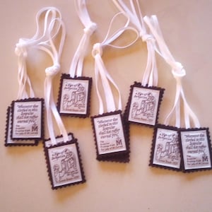 May include: Several small, rectangular religious pendants with white ribbon ties. Each pendant has a dark border and a printed image with text. The text includes the words "Scapular" and "eternal fire".