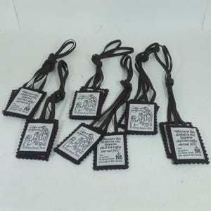 May include: A collection of black scapulars, each with a rectangular white tag featuring an illustration and text. The tags are connected to black cords. The text includes phrases like "A Sign of Salvation" and "Our Lady of Mt. Carmel."
