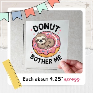 K&ouml;nnte beinhalten: Wei&szlig;er Aufkleber mit einem Cartoon-Faultier, das auf einem rosa Donut mit Streuseln schl&auml;ft. Der Text "DONUT BOTHER ME" ist um den Donut geschrieben. Der Aufkleber ist etwa 10,8 cm breit.