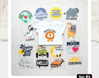 May include: A white baby bodysuit featuring a central lion graphic with the text MIGHTY CUTE, surrounded by twelve assorted iron-on transfers including a globe, rainbow, elephant, giraffe, zebra, jeep, sheep, sloth, and various sun and text designs.