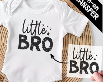 May include: A white short-sleeved baby bodysuit featuring the black text "little BRO" with small star accents. A separate transparent sheet displays the same "little BRO" design, indicating an iron-on transfer application for the garment.