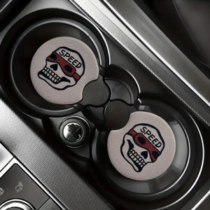 May include: Two gray car coasters with a skull design and the word "SPEED" in red letters. The skull is wearing red goggles.