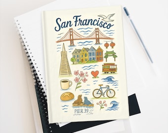 May include: A notebook with a cream-colored cover featuring a colorful illustration of San Francisco landmarks, including the Golden Gate Bridge, painted ladies, and a cable car. The text "San Francisco" is written across the top.