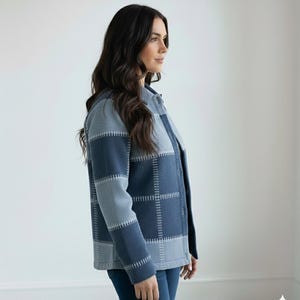 May include: A blue and grey patchwork jacket with a button-up front. The jacket has a plaid design with visible stitching. The sleeves are long, and the jacket is worn with blue jeans. The overall style is casual and comfortable.
