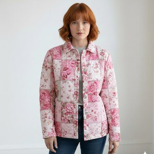 Op de afbeelding: Een roze gewatteerde jas met een patchwork-ontwerp met bloempatronen. De jas heeft een knoopsluiting aan de voorkant, een kraag en lange mouwen. De bloemenprint bevat tinten roze en wit.