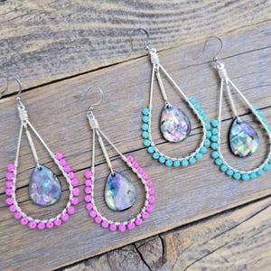 May include: Two pairs of teardrop-shaped wire earrings. One pair features bright pink beads along the lower wire frame, while the other pair has turquoise beads. Each earring contains a central iridescent, dark, pear-shaped stone pendant.