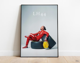 Könnte beinhalten: Gerahmter Druck mit einer Person in einem roten Rennanzug, die auf einem Reifen sitzt. Das Bild enthält einen gelben Helm und den Text "LH44" oben. Die Person trägt rote Schuhe und eine Uhr.