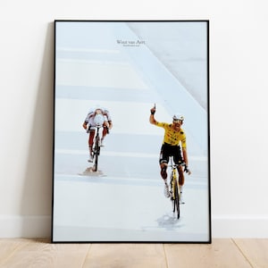 Peut inclure: Impression encadrée représentant deux cyclistes en pleine course. L'un, en maillot jaune, lève le bras en signe de victoire. L'autre porte un maillot blanc et rouge. Le texte "Wout van Aert" est en haut.
