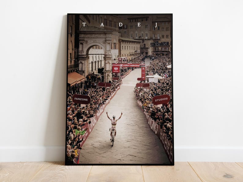 May include: A black and white photo of a cyclist raising their arms in victory as they cross the finish line of a race. The cyclist is wearing a white jersey with red and blue accents. The photo is taken from a high angle, looking down on the cyclist and the crowd of spectators lining the street. The street is lined with red and white banners and signs. The photo is titled "TADEJ" in white letters at the top.