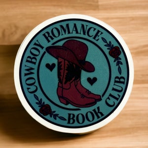 Puede incluir: Pegatina redonda con el texto "COWBOY ROMANCE BOOK CLUB". El diseño presenta un fondo turquesa con un sombrero y botas de vaquero burdeos. Corazones y rosas adornan el conjunto, con un borde blanco.