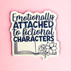 Puede incluir: Pegatina blanca con texto azul que dice "Emocionalmente apegado a los personajes ficticios". La pegatina presenta una ilustración en blanco y negro de un libro abierto con flores.