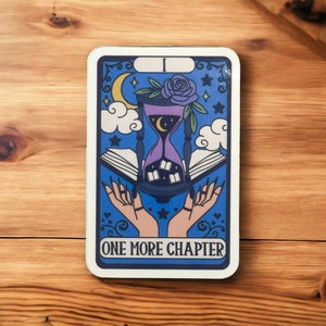 Puede incluir: Una carta de tarot azul con borde blanco y el texto "One More Chapter". La carta presenta una ilustración de un reloj de arena con un libro y una mano extendida.